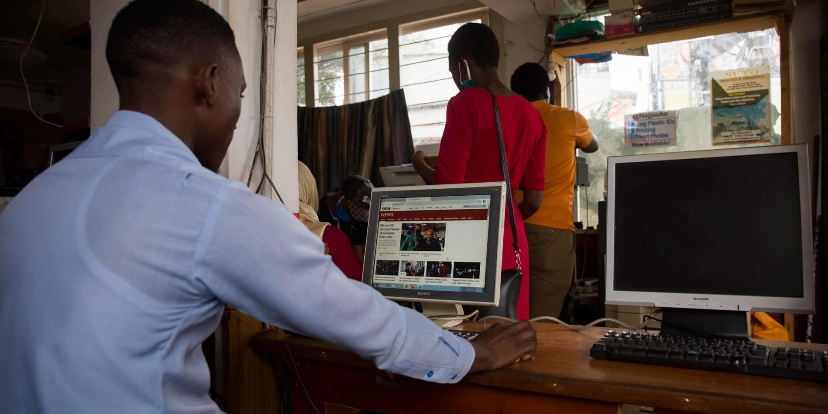 An African man sits behind a computer reading a newspaper online.