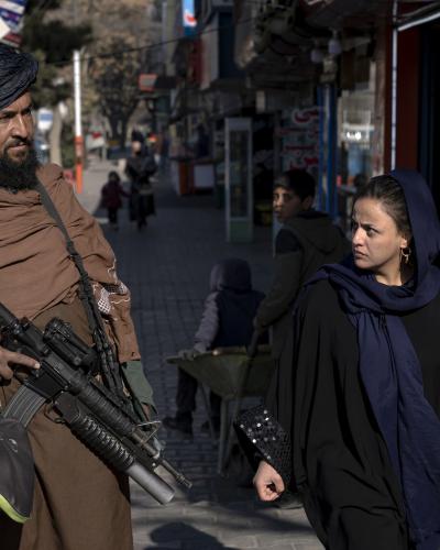 A Taliban fighter stands guard as a woman walks past him in Kabul.