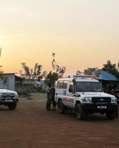 Two white off-road vehicles labelled "UN" and "Ambulance" are parked in a sandy square. © UN Photo